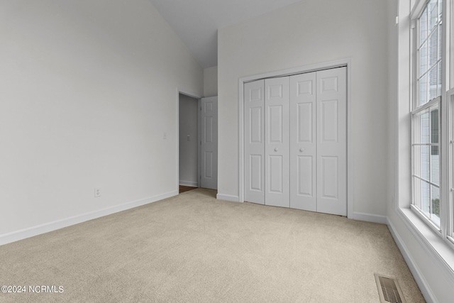 unfurnished bedroom with light carpet, high vaulted ceiling, and a closet