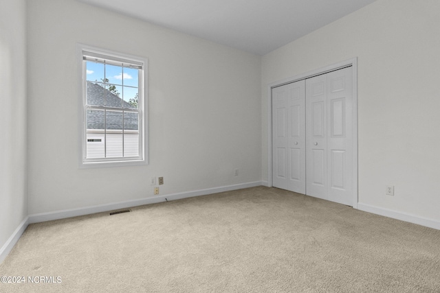 unfurnished bedroom with light colored carpet and a closet