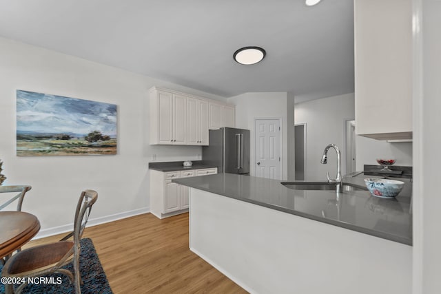 kitchen with high quality fridge, white cabinetry, sink, kitchen peninsula, and light hardwood / wood-style flooring