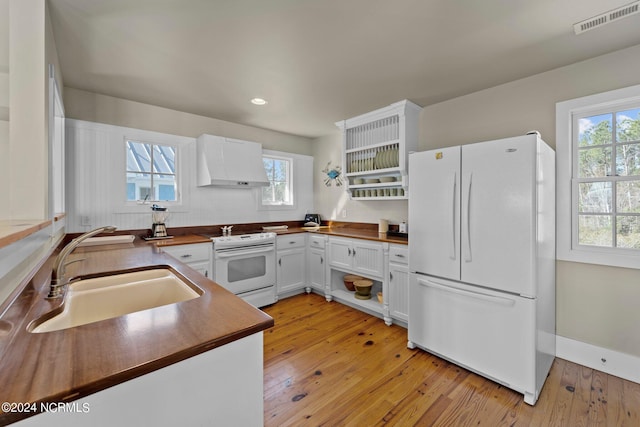 kitchen featuring light wood-type flooring, white appliances, wall chimney range hood, sink, and white cabinets