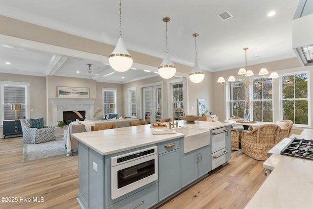 kitchen with light wood finished floors, gray cabinets, visible vents, a high end fireplace, and a sink