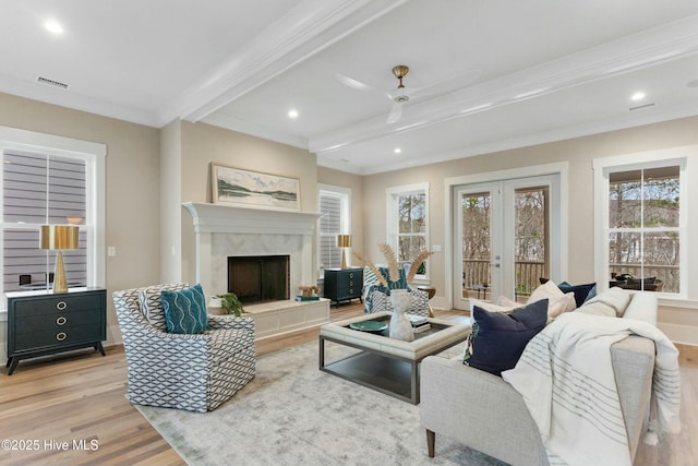 living area with a fireplace, visible vents, light wood-style floors, french doors, and beamed ceiling