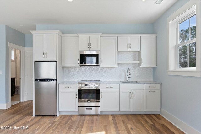 kitchen featuring stainless steel appliances, light wood-style flooring, decorative backsplash, white cabinets, and a sink