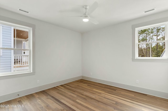 spare room with a ceiling fan, wood finished floors, visible vents, and baseboards