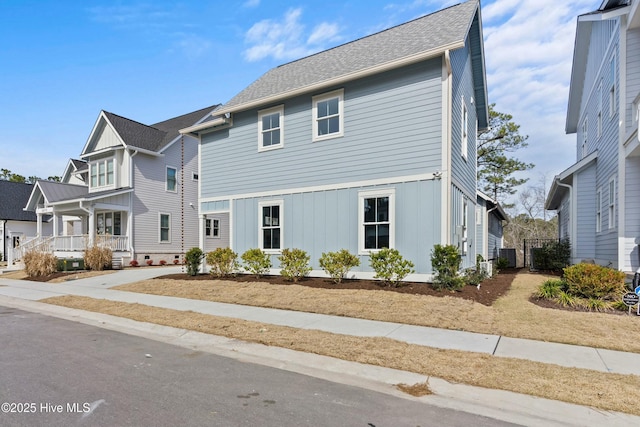 view of front of house featuring board and batten siding, a residential view, cooling unit, and a shingled roof