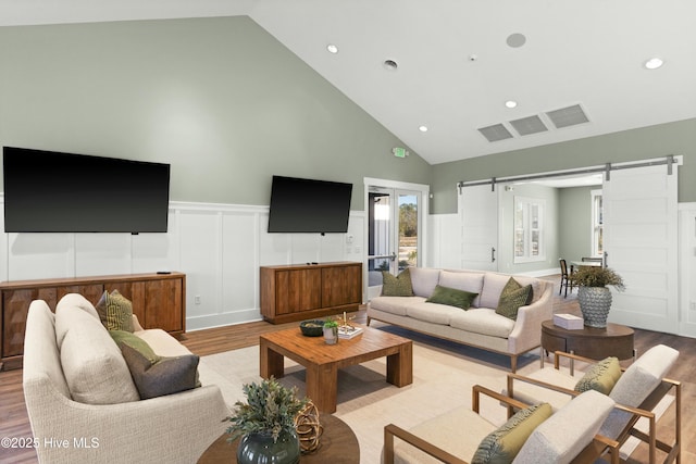 living area with recessed lighting, a barn door, wainscoting, wood finished floors, and high vaulted ceiling