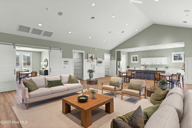 living room featuring recessed lighting, visible vents, a barn door, high vaulted ceiling, and light wood-type flooring