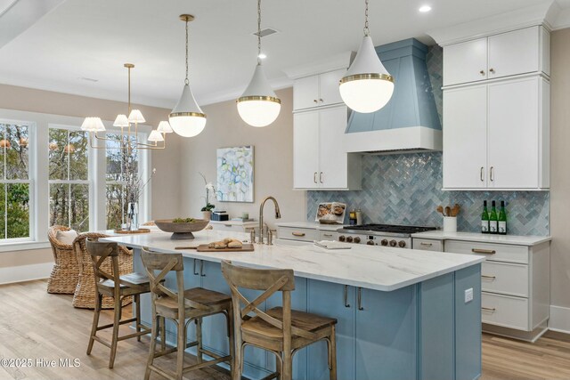 kitchen with tasteful backsplash, premium range hood, light stone countertops, and white cabinets