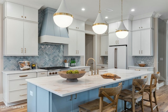 kitchen featuring stainless steel gas cooktop, visible vents, custom exhaust hood, freestanding refrigerator, and a kitchen bar