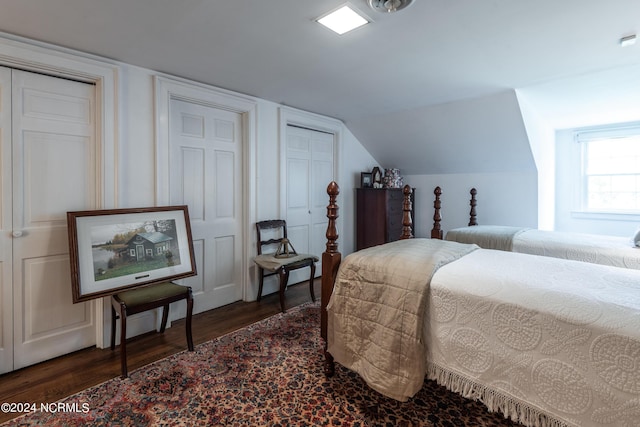 bedroom with dark hardwood / wood-style floors, lofted ceiling, and two closets