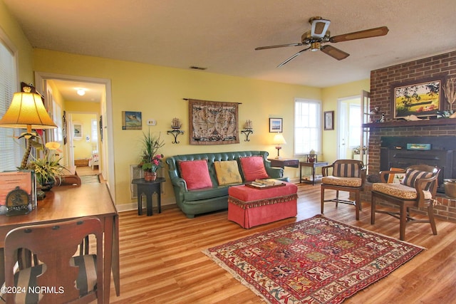 living room featuring a brick fireplace, hardwood / wood-style flooring, a textured ceiling, and ceiling fan