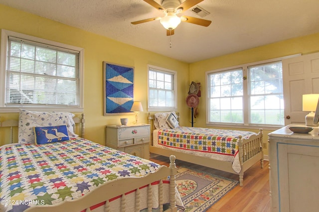 bedroom with ceiling fan, light hardwood / wood-style flooring, and a textured ceiling