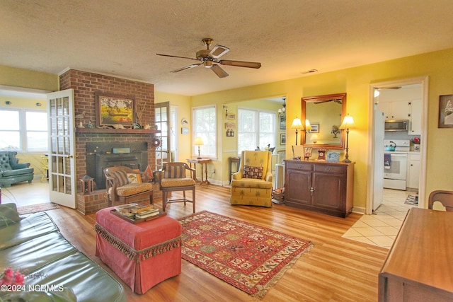 living room with a brick fireplace, light hardwood / wood-style floors, a textured ceiling, and ceiling fan