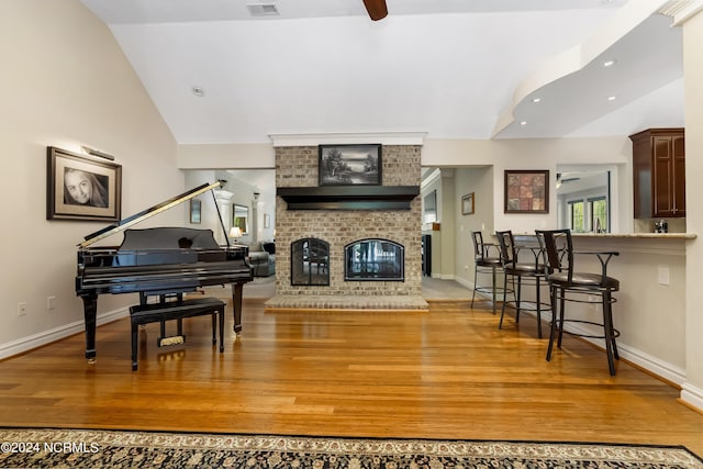 sitting room with lofted ceiling, a brick fireplace, light wood finished floors, and a ceiling fan