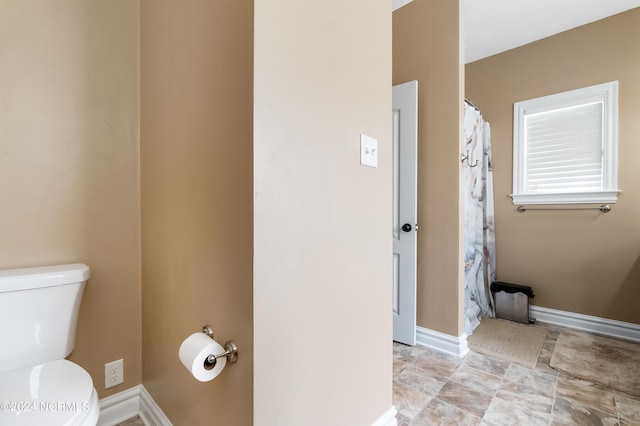 bathroom featuring a shower with shower curtain, toilet, and baseboards