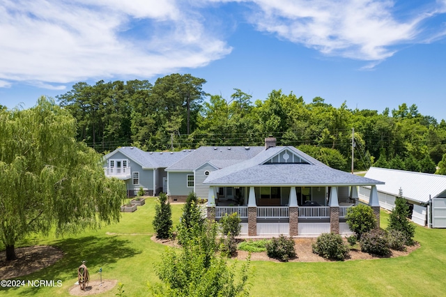 rear view of property featuring a porch, a yard, a chimney, and a shingled roof