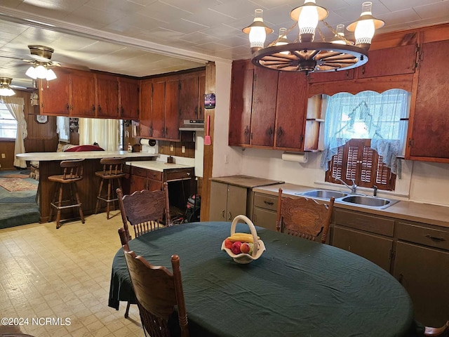 kitchen with decorative light fixtures, ceiling fan with notable chandelier, kitchen peninsula, a kitchen bar, and sink