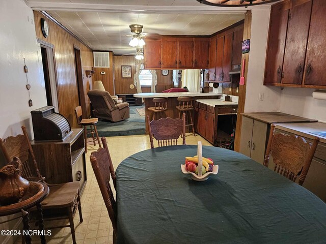 dining area with crown molding, wooden walls, ceiling fan, and light colored carpet