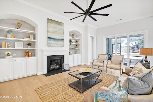 living room with built in shelves, ceiling fan, crown molding, and light hardwood / wood-style floors