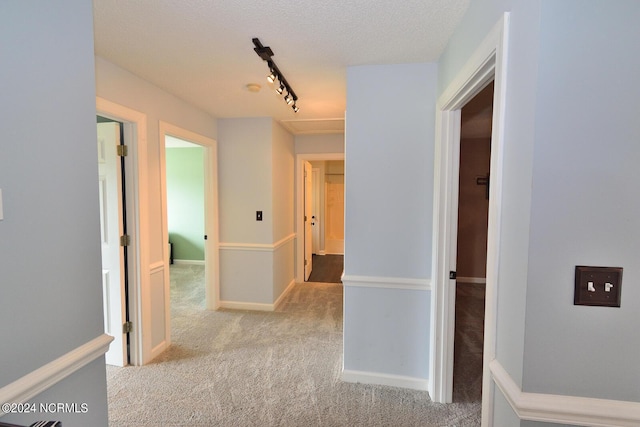 corridor with a textured ceiling, light colored carpet, and rail lighting