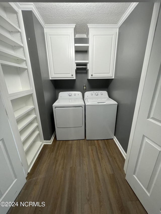 laundry room featuring cabinets, crown molding, a textured ceiling, dark hardwood / wood-style flooring, and washing machine and clothes dryer