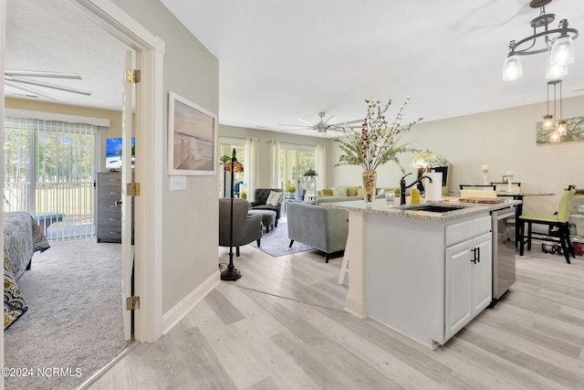 kitchen with white cabinets, pendant lighting, light hardwood / wood-style flooring, ceiling fan, and sink