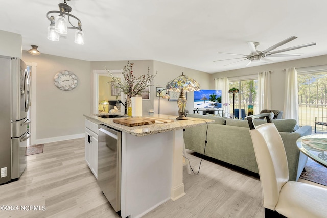 kitchen with light hardwood / wood-style floors, white cabinets, ceiling fan with notable chandelier, stainless steel appliances, and sink