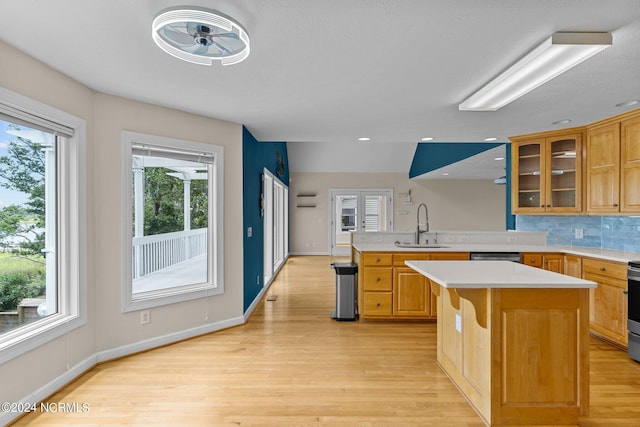 kitchen featuring sink, kitchen peninsula, decorative backsplash, a kitchen island, and light wood-type flooring