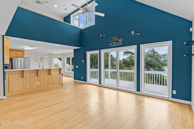 unfurnished living room featuring ceiling fan, sink, light hardwood / wood-style floors, and a high ceiling