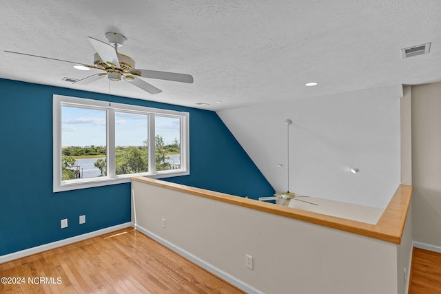 additional living space with a textured ceiling, ceiling fan, light hardwood / wood-style flooring, and vaulted ceiling