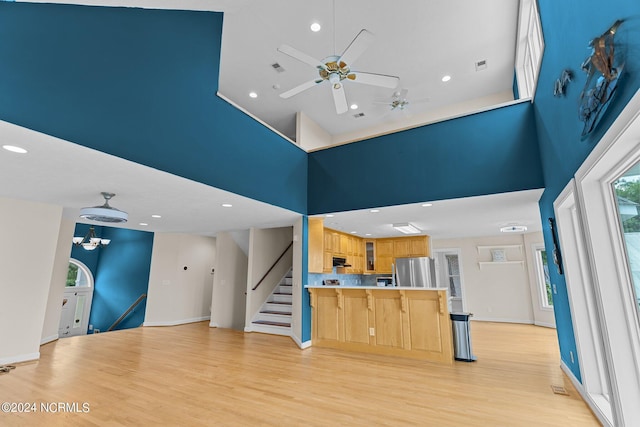 unfurnished living room featuring ceiling fan with notable chandelier, light hardwood / wood-style floors, and a high ceiling