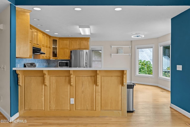 kitchen featuring decorative backsplash, light hardwood / wood-style floors, a kitchen bar, kitchen peninsula, and stainless steel appliances