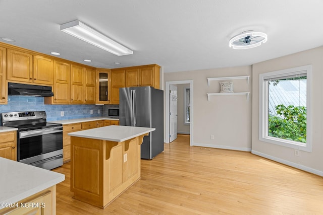 kitchen with decorative backsplash, appliances with stainless steel finishes, a kitchen breakfast bar, light hardwood / wood-style flooring, and a center island