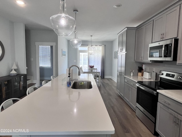 kitchen with gray cabinets, dark hardwood / wood-style floors, sink, a center island with sink, and appliances with stainless steel finishes