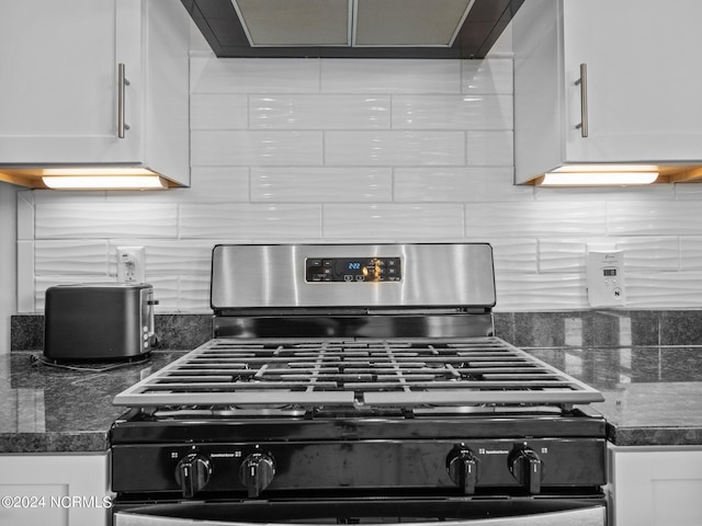 details with dark stone countertops, white cabinetry, range hood, and stainless steel gas range