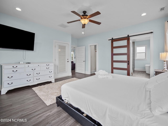 bedroom with a barn door, dark hardwood / wood-style floors, ensuite bath, and ceiling fan