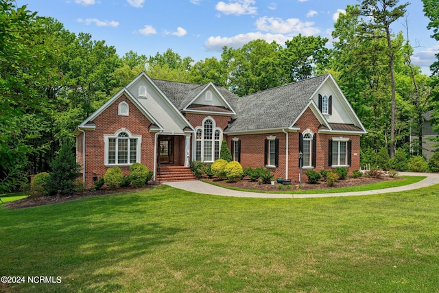 view of front of home featuring a shingled roof, a front yard, and brick siding