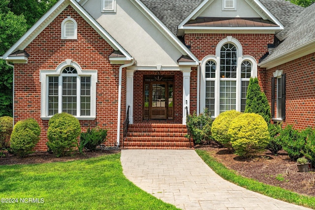 view of exterior entry with brick siding, stucco siding, a shingled roof, a standing seam roof, and metal roof