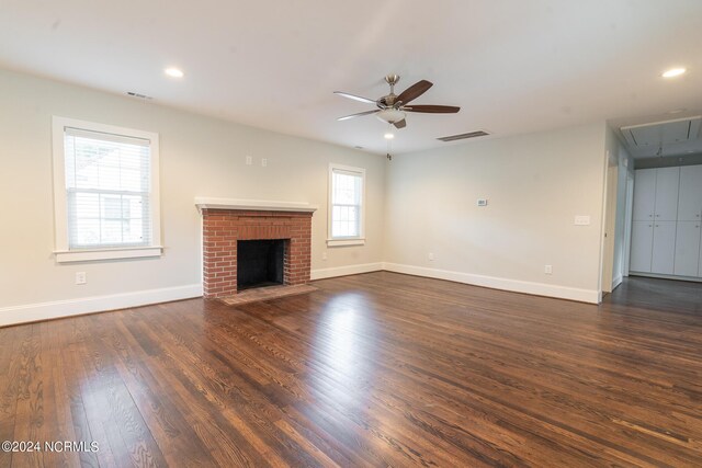 unfurnished living room with a healthy amount of sunlight, dark hardwood / wood-style floors, a brick fireplace, and ceiling fan