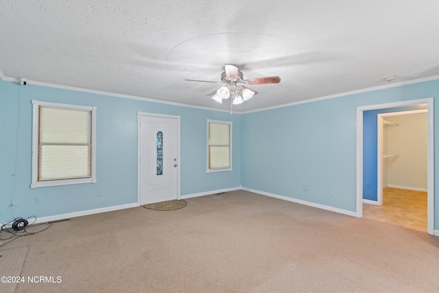 unfurnished living room featuring ceiling fan, ornamental molding, a textured ceiling, and carpet