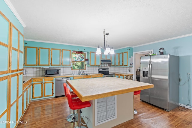 kitchen featuring stainless steel appliances, a center island, light hardwood / wood-style floors, a kitchen bar, and decorative light fixtures