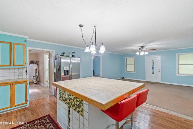 kitchen featuring hanging light fixtures, stainless steel fridge, light hardwood / wood-style floors, and tile countertops