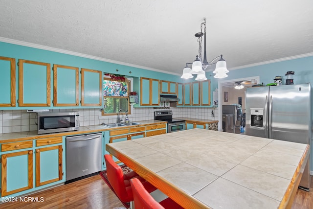 kitchen with pendant lighting, stainless steel appliances, tile countertops, and sink