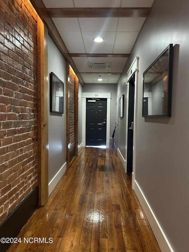 hallway featuring a paneled ceiling, brick wall, and dark hardwood / wood-style floors