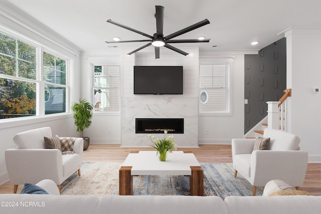 living room with a fireplace, light hardwood / wood-style floors, ceiling fan, and crown molding