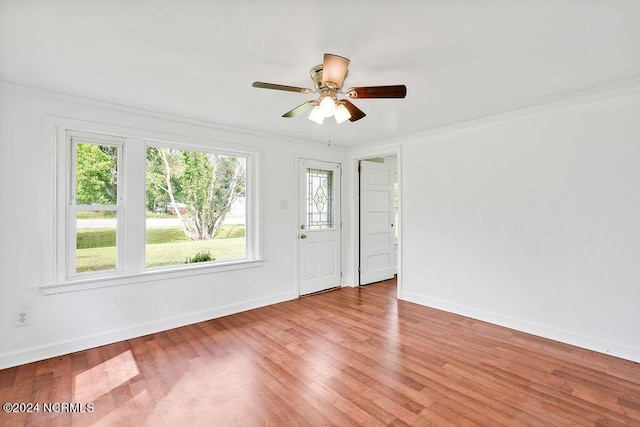 empty room with ornamental molding, wood finished floors, a ceiling fan, and baseboards