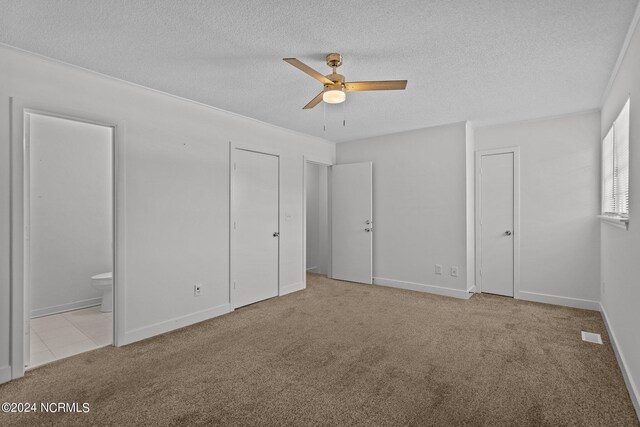 unfurnished bedroom with ensuite bath, ceiling fan, light colored carpet, and a textured ceiling