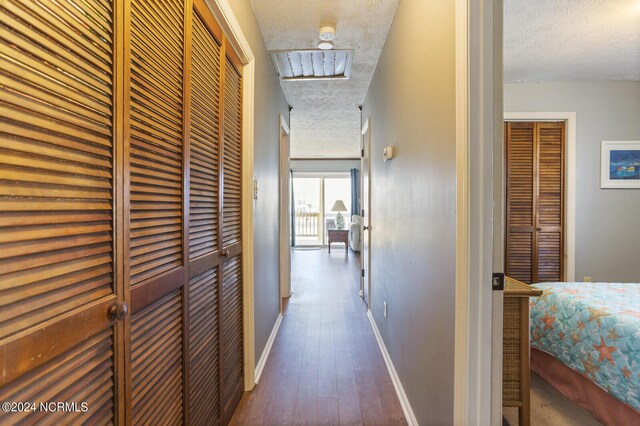 corridor with a textured ceiling and dark hardwood / wood-style flooring