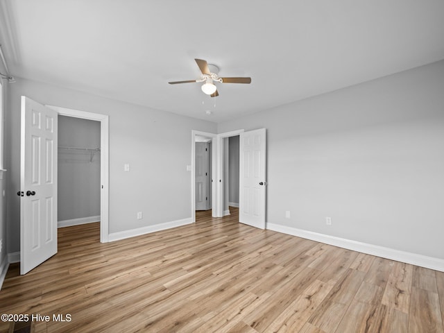 unfurnished bedroom with a walk in closet, a closet, ceiling fan, and light wood-type flooring