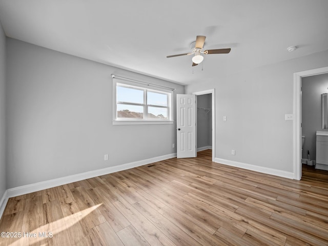 unfurnished bedroom featuring a spacious closet, a closet, ceiling fan, and light wood-type flooring